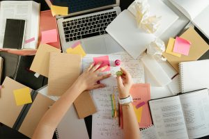 A cluttered desk with notebooks, sticky notes, and a laptop, depicting a student's busy life.