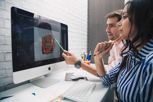 Side view of focused coworkers working together on graphic design while sitting at table and looking at monitor in modern office
