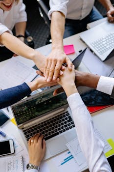 A diverse group of professionals stacking hands over a table symbolizing teamwork and collaboration.