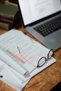 Glasses and documents on a desk with a laptop, representing a busy workspace.